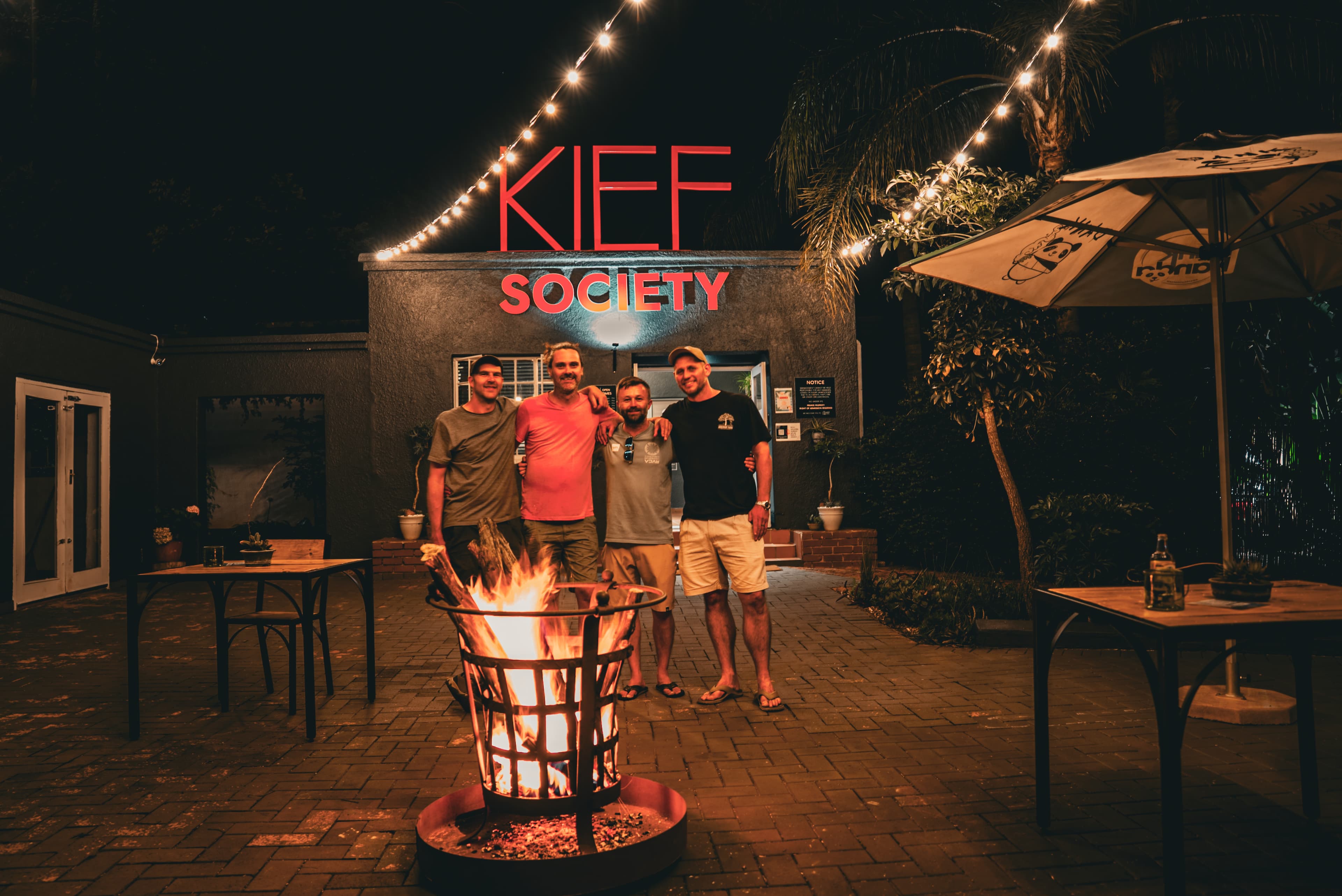 Kief Society at night — members gathered around the fire pit at the entrance